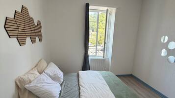 Een slaapkamer met een bed, een raam, een kunstwerk aan de muur en een kleine plant.