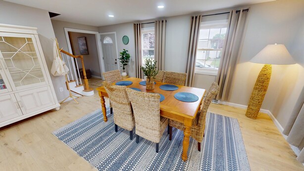 Uma sala de jantar com uma mesa de madeira, cadeiras de vime e um tapete estampado.