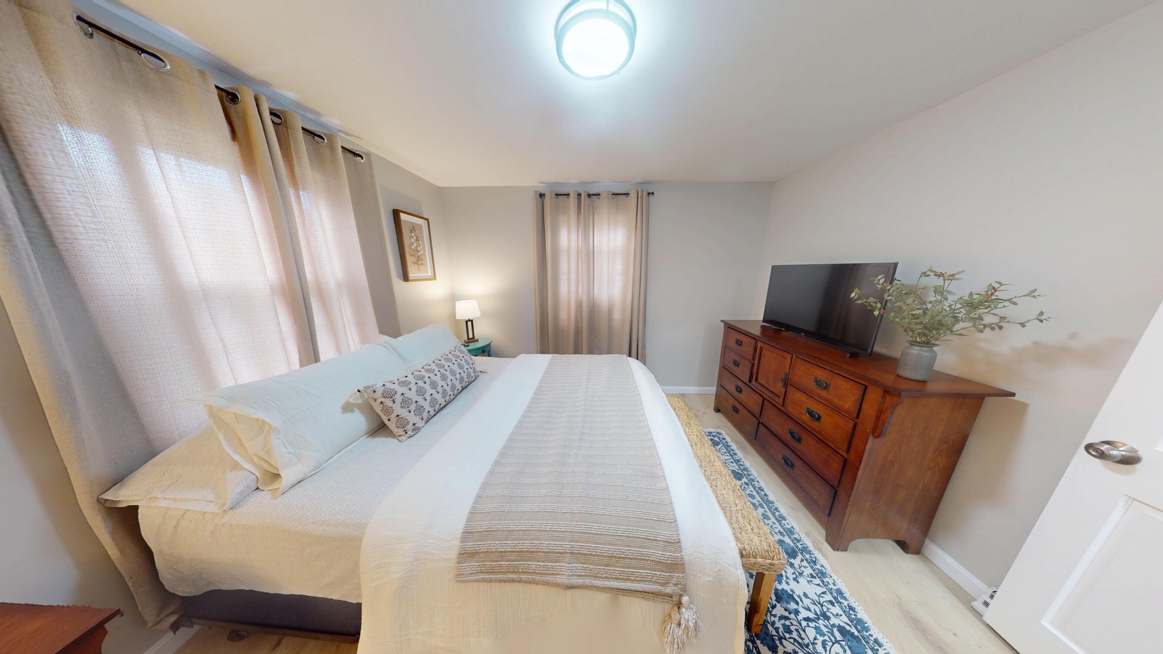 Une chambre d’hôtel avec un lit, une commode en bois, un téléviseur et une petite table avec une lampe.