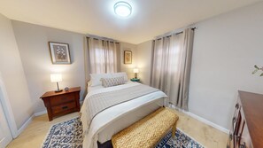 Una habitación de hotel con cama, mesitas de noche, lámpara, alfombra pequeña y un banco.