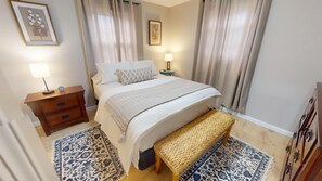 A bedroom with a bed, bedside tables, a lamp, a clock, and a woven bench.