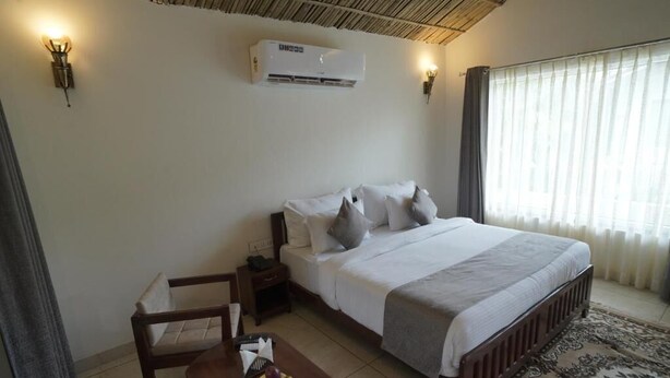 A bedroom with a bed, bedside table, chair, and a window with curtains. - Amar Bagh Resort Pushkar (Pushkar)