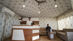 A reception area with a wooden reception desk, a ceiling fan, and patterned wallpaper. - Amar Bagh Resort Pushkar (Pushkar)