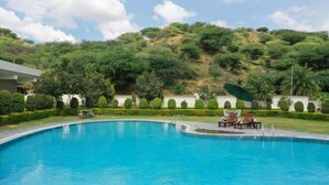 A swimming pool with lounge chairs and a table, surrounded by neatly trimmed hedges and a hillside backdrop. - Amar Bagh Resort Pushkar (Pushkar)