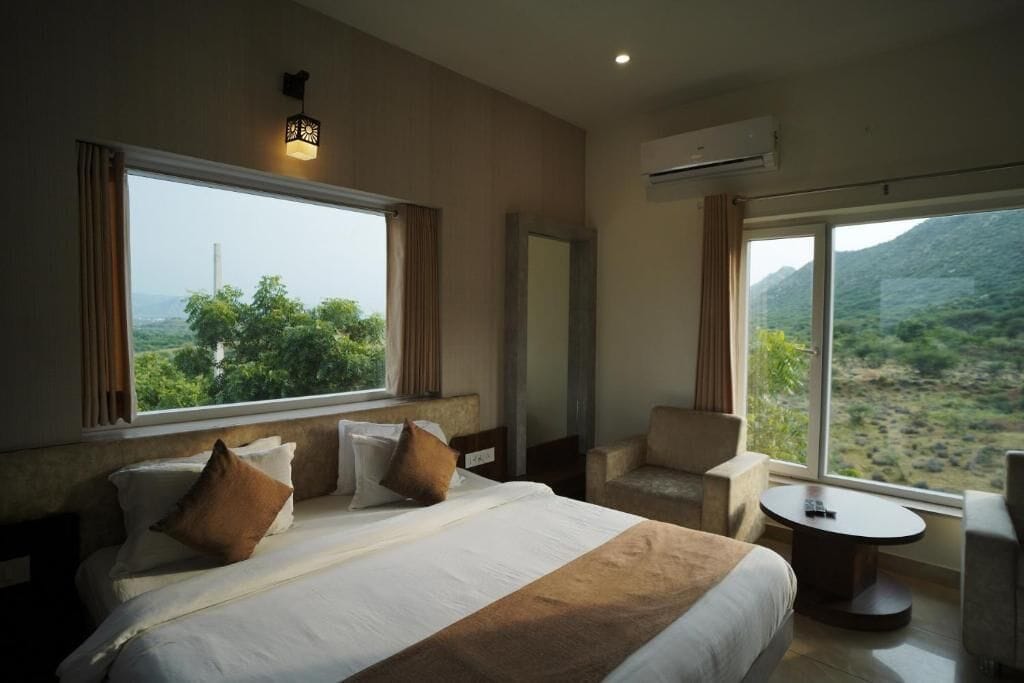 A hotel room with a large bed, a sitting area with a table, and a view of a mountainous landscape.