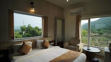 A hotel room with a large bed, a sitting area with a table, and a view of a mountainous landscape.