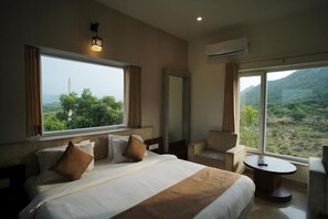 Habitación de hotel con una cama grande, un área de descanso con una mesa y vistas a un paisaje montañoso.