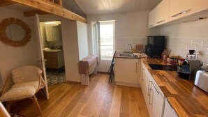 A kitchen with wooden flooring, a dining area with a chair, and a view of the adjacent bathroom. - A cozy little retreat on Penotte Island (Les Sables-d'Olonne)