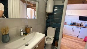 A bathroom with a white sink, a toilet, and a mirror reflecting a room with a TV and kitchen area. - A cozy little retreat on Penotte Island (Les Sables-d'Olonne)