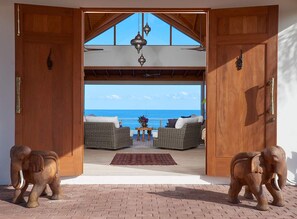 Eine Holztür führt auf einen Balkon mit Korbmöbeln und Blick aufs Meer.