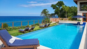 A rectangular swimming pool with a clear blue water, surrounded by lounge chairs and a view of the ocean. - Tropical-inspired 5BR Modern Seafront Villa Infinity Pool Direct Sea Access (Boscobel)