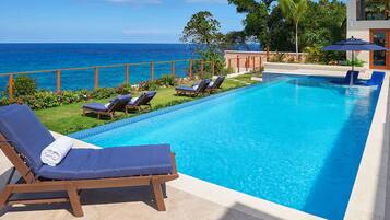 A rectangular swimming pool with a clear blue water, surrounded by lounge chairs and a view of the ocean.