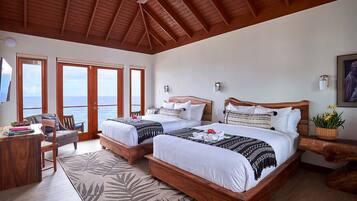 A hotel room with two beds, a desk, and a chair. There are large windows with a view of the sea.