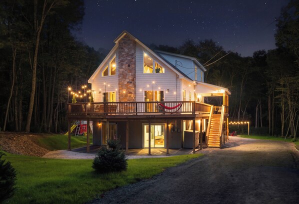 A two-story house with a stone facade, a balcony with string lights, and a visible garage.