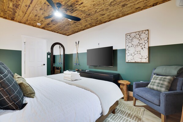 A bedroom with a bed, a chair, a television, and a ceiling fan.