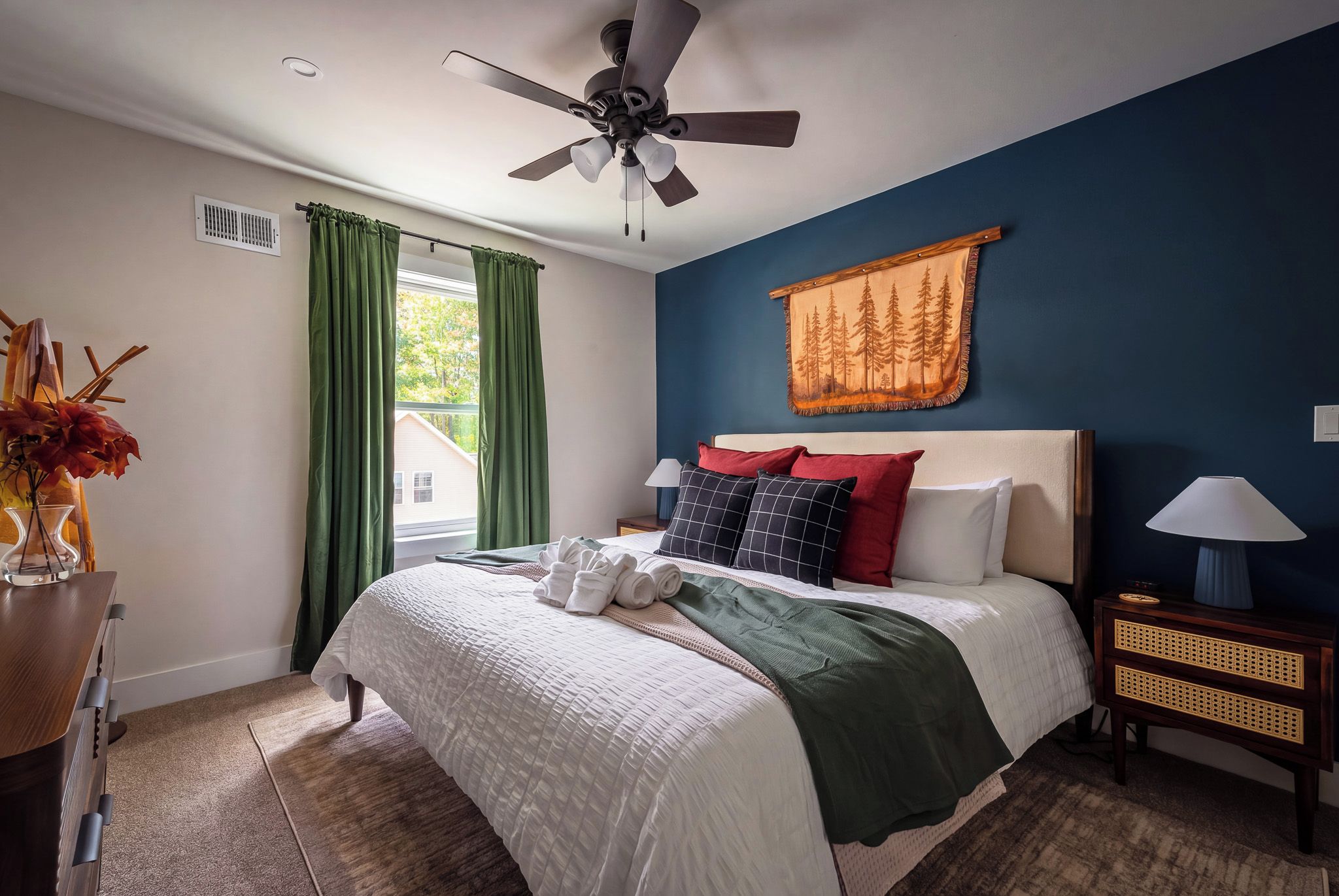 Une chambre à coucher comprenant un lit, une table de chevet, une lampe, un ventilateur de plafond et une fenêtre avec des rideaux.