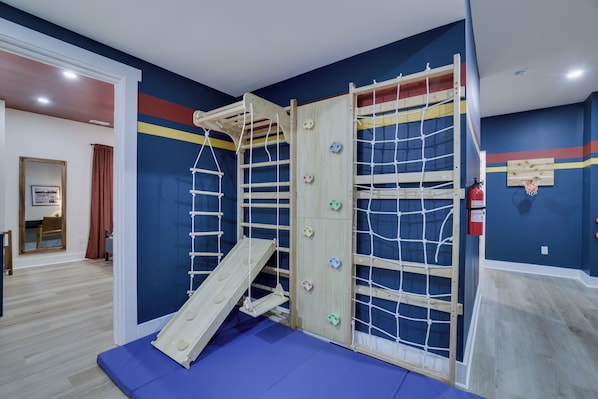 A play area with a wooden climbing structure, a slide, and a blue mat.