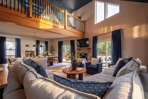 A spacious living room with a high ceiling, a staircase, a fireplace, and a dining area.