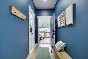 A hallway with a wooden bench, a green rug, and a door leading to an outdoor area with a wooden deck.