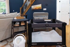 A room with a blue wall, a white door, a grey playpen, a white baby rocker, a grey chair, and a grey sofa.