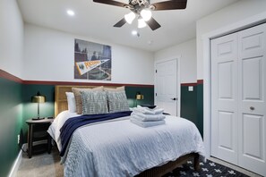 A bedroom with a bed, a nightstand, a lamp, a ceiling fan, and a door.