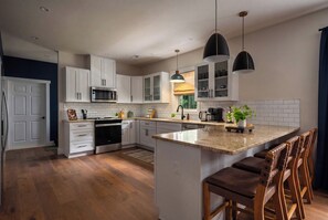 A modern kitchen with white cabinetry, a central island, bar stools, and pendant lighting.
