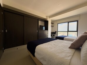 A bedroom with two beds, a dark wardrobe, a TV, and a window with a city view. - Spectacular Oceanview Escape in Torre 5 | Minutes to Centro! (Mazatlan)