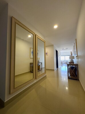 A hallway with large mirrors, a tiled floor, and a view into a room with a bed and a window. - Spectacular Oceanview Escape in Torre 5 | Minutes to Centro! (Mazatlan)