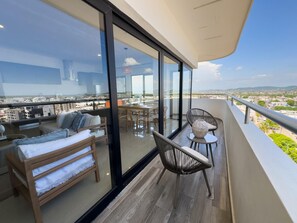 A balcony with a sofa, chairs, and a table, overlooking a cityscape. - Spectacular Oceanview Escape in Torre 5 | Minutes to Centro! (Mazatlan)
