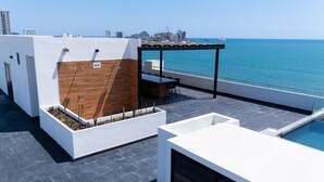 A rooftop terrace with a pool, seating area, and a view of the sea. - Spectacular Oceanview Escape in Torre 5 | Minutes to Centro! (Mazatlan)