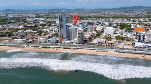 A coastal cityscape with a beach, high-rise buildings, and a prominent red location marker. - Spectacular Oceanview Escape in Torre 5 | Minutes to Centro! (Mazatlan)