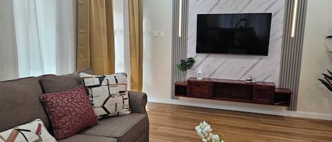 A modern living room with a sofa, a coffee table with a plant, a TV mounted on a marble wall, and a wooden floor.