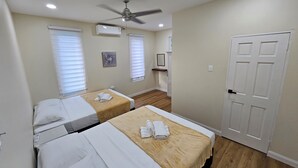 Habitación de hotel con dos camas, ventilador de techo, aire acondicionado y una puerta.
