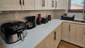 Una cocina con gabinetes blancos, cafetera, tostadora y lavamanos.