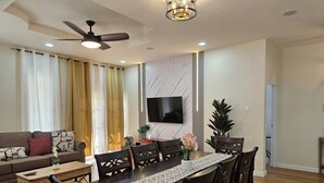Una sala de estar moderna con comedor, un juego de sofá, un televisor montado en la pared y un ventilador de techo.