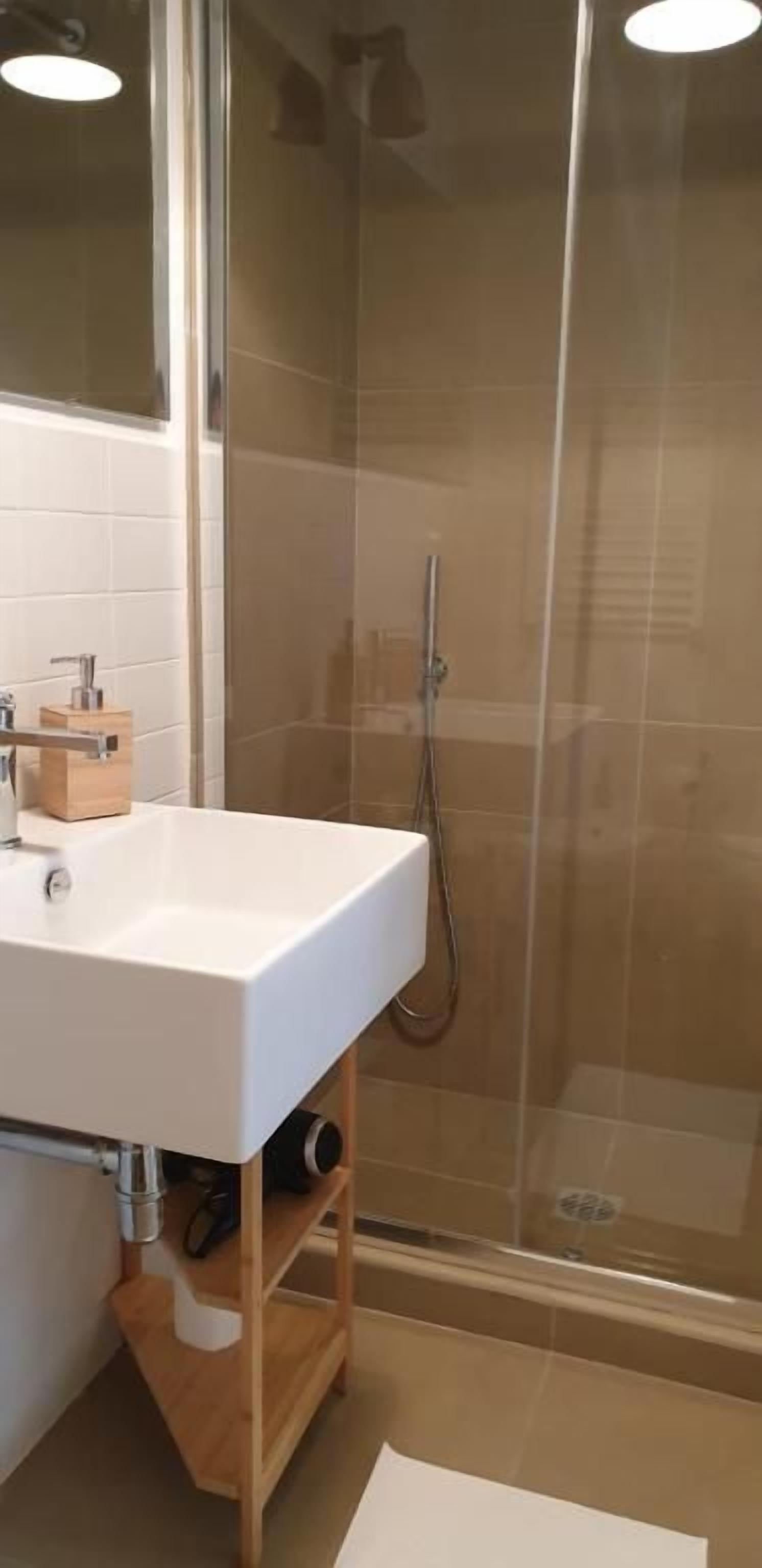 Ein Badezimmer mit einem weißen Waschbecken, einem Holzschrank und einer Duschkabine aus Glas.