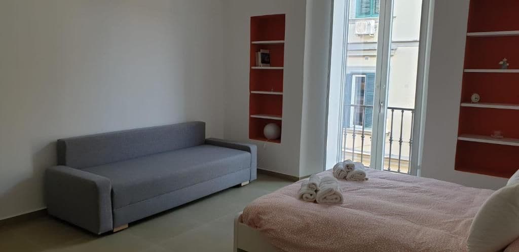 Una habitación con un sofá gris, una cama con ropa de cama rosa y estanterías rojas.