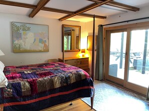 A bedroom with a large bed, a dresser, a mirror, and a sliding glass door leading to an outdoor area.
