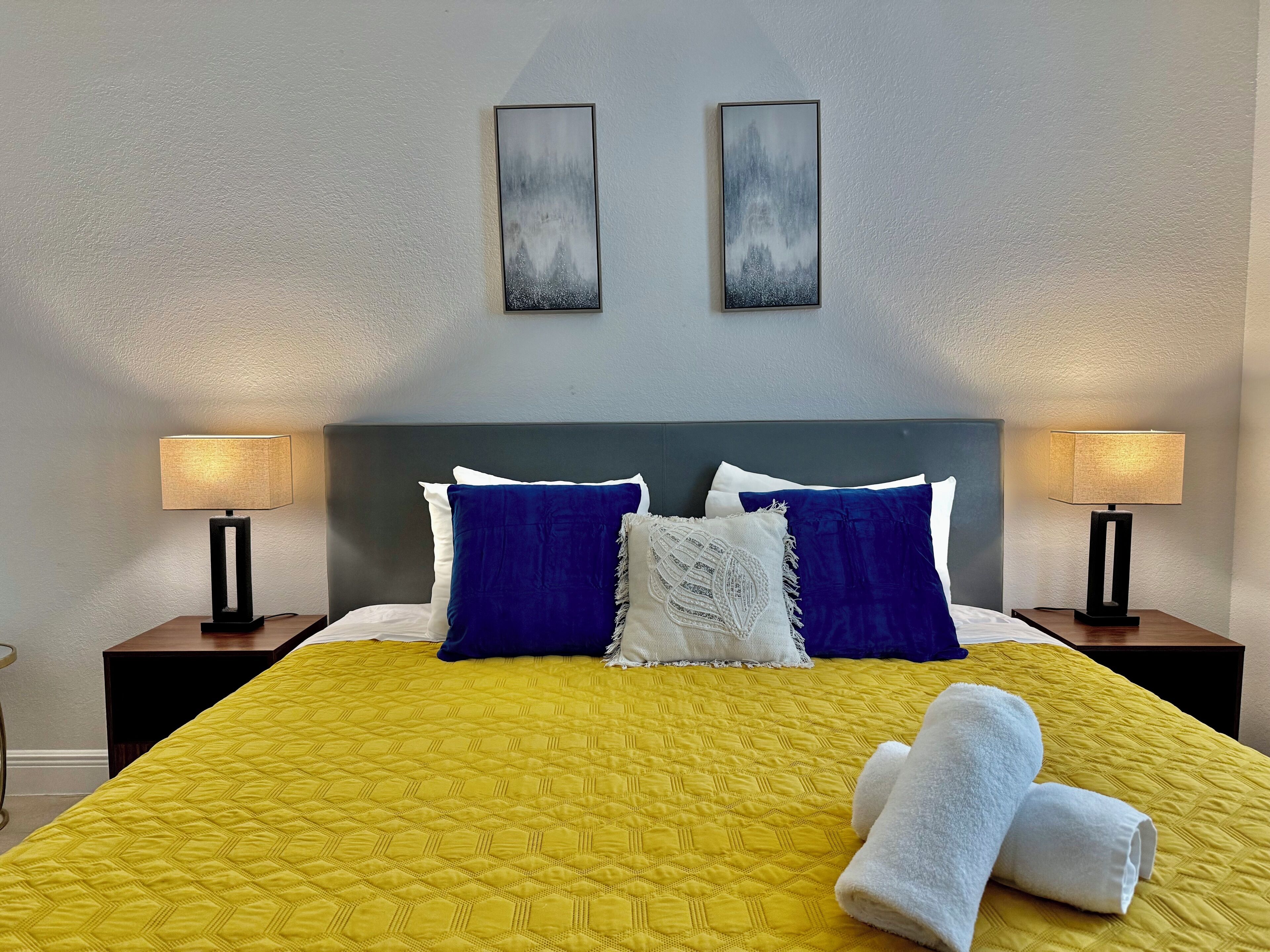 Habitación de hotel con una cama grande, dos lámparas de noche y dos cuadros en la pared.