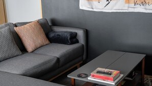 A modern living room with a grey sofa, patterned pillows, a coffee table with books and a remote control, and a grey carpet. - Casa Maryna. (Villa de Cos)