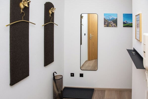 A hallway with a mirror, two wall-mounted hooks, a door, and a small shelf with a framed certificate.