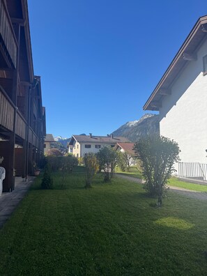 A residential area with a grassy courtyard, wooden buildings, and a mountain in the background.