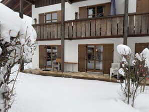A two-story building with wooden balconies, a covered outdoor seating area, and snow-covered surroundings.