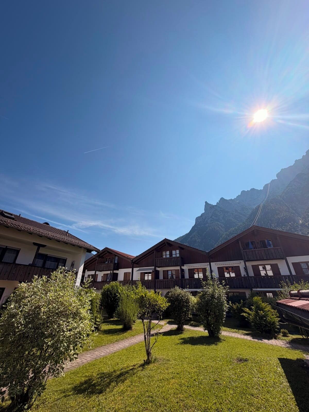 A hotel courtyard with a mountain backdrop, featuring a clear sky and a sun shining.