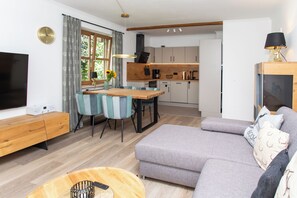 A modern living room with a grey sofa, a wooden coffee table, and a TV on the left.