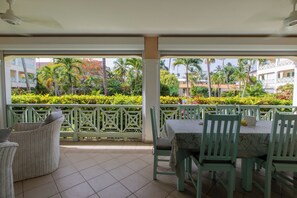 A covered outdoor seating area with a view of a landscaped garden and buildings in the background. - Bamboo House, Oceanfront, Las Terrenas, Punta Popi. Comfort, convenience, and magic. (Las Terrenas)