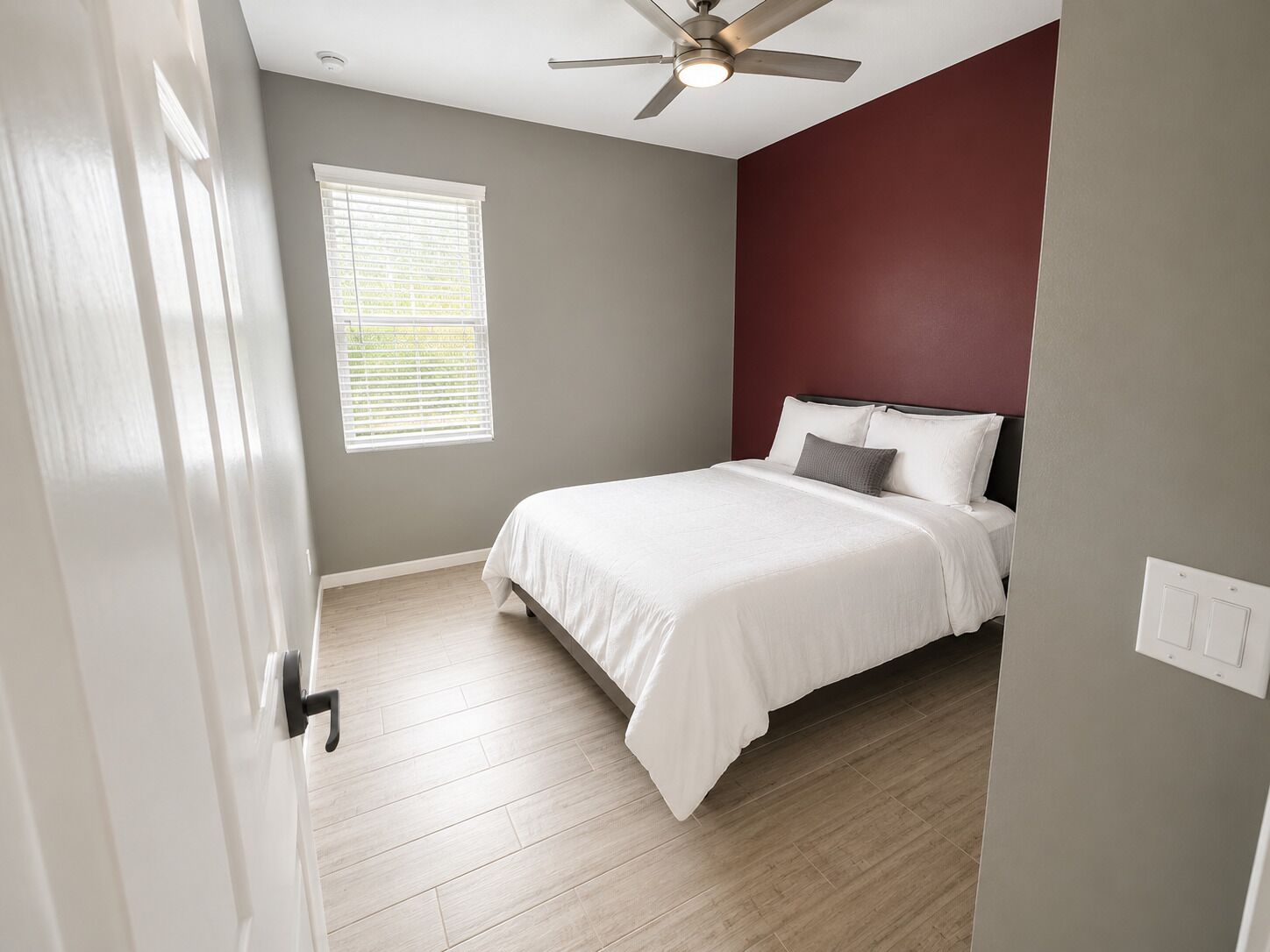 A bedroom with a bed, a ceiling fan, a window with blinds, and a door.