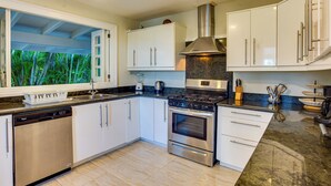 A modern kitchen with white cabinets, a stainless steel stove, and a window with a tropical view. - Tortuga C20 Luxury 5-Bedroom Villa at the Punta Cana Resort (Punta Cana)
