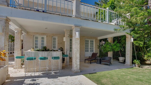 A covered outdoor seating area with chairs and a table, a balcony with a railing, and a view of a lush garden. - Tortuga C20 Luxury 5-Bedroom Villa at the Punta Cana Resort (Punta Cana)