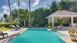 A pool area with lounge chairs, a covered seating area, and a view of a lush garden. - Tortuga C20 Luxury 5-Bedroom Villa at the Punta Cana Resort (Punta Cana)